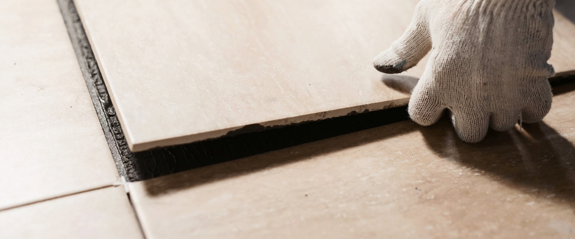 Die Hände des Fliesenlegers verlegen die Keramikfliesen auf dem Boden. Nahaufnahme im Makroformat. Hausrenovierung und Bau eines neuen Hauses Konzept
